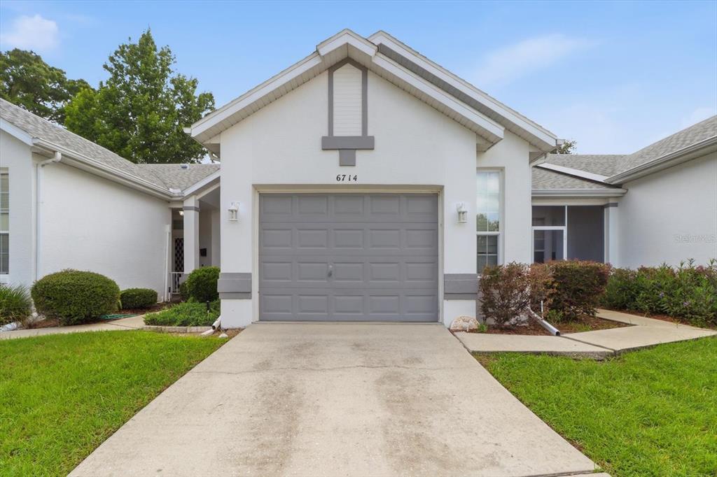 A single-story house exterior features a gray garage door, white stucco walls, and a driveway — 6714 E WAYBRIDGE COURT, INVERNESS, FL