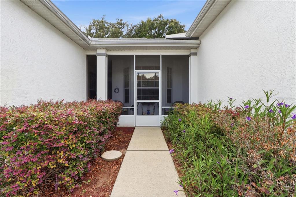 A concrete walkway leads to a screened-in entryway flanked by bushes and white walls — 6714 E WAYBRIDGE COURT, INVERNESS, FL