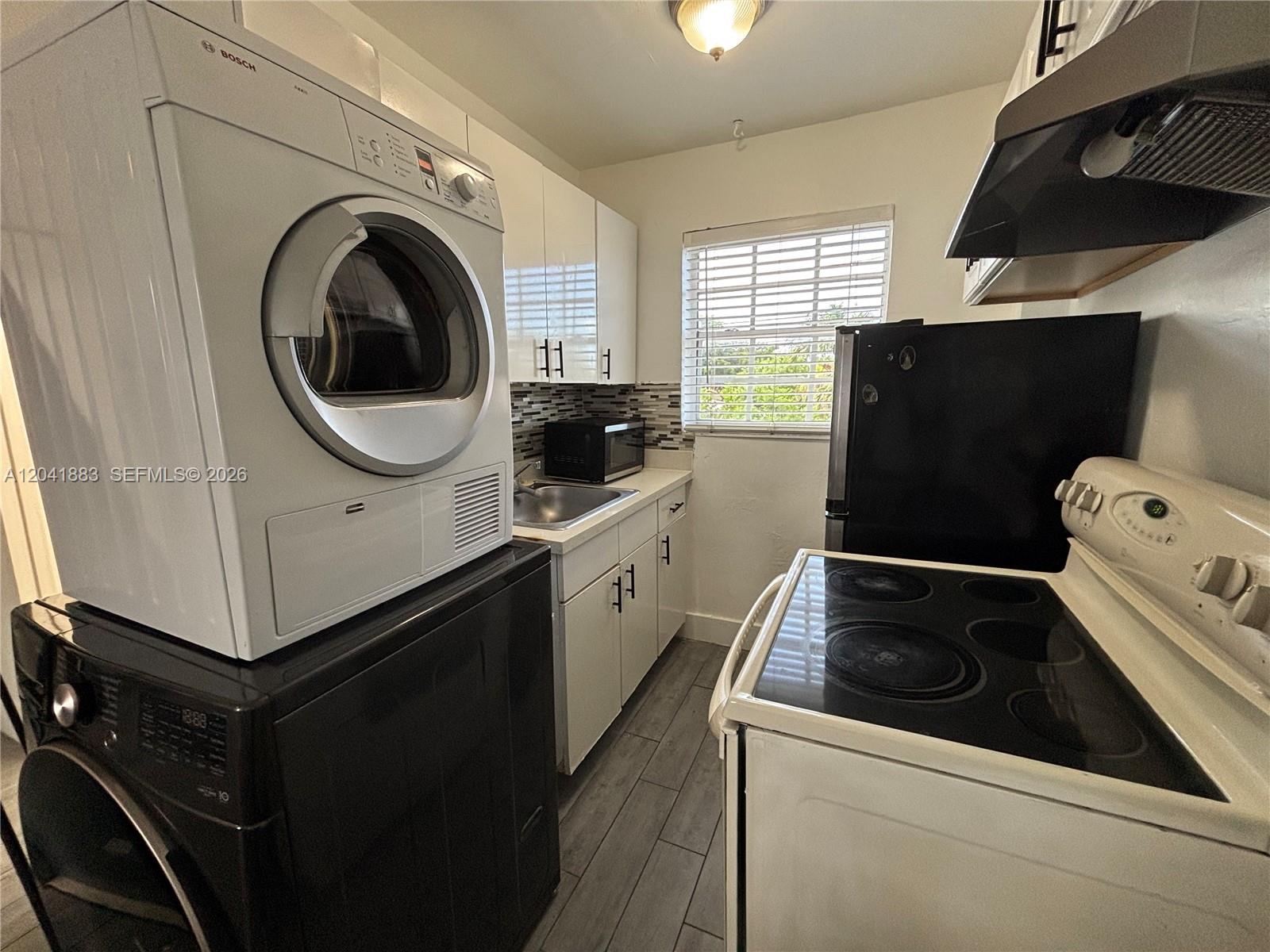 A small kitchen features a stacked washer and dryer, white cabinets, and black appliances — 1843 Dewey St # 114, Hollywood FL 33020, HOLLYWOOD, FL