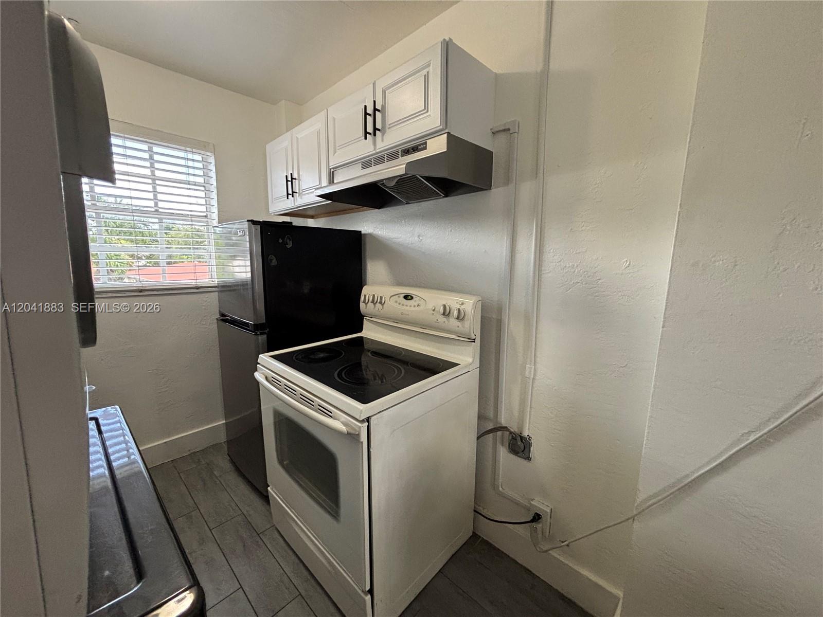 A small kitchen features a white electric stove, a black refrigerator, and white upper cabinets — 1843 Dewey St # 114, Hollywood FL 33020, HOLLYWOOD, FL
