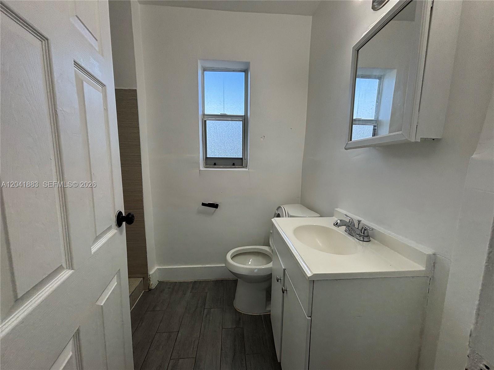 A small bathroom features a white vanity, a toilet, a window, and wood-look tile flooring — 1843 Dewey St # 114, Hollywood FL 33020, HOLLYWOOD, FL