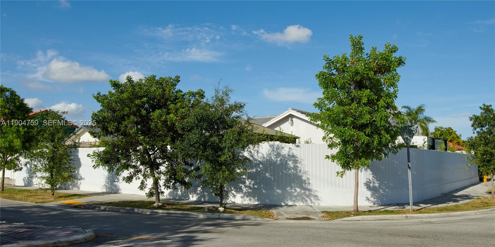 A white fence surrounds a house with trees in the foreground under a blue sky — 2980 SW 141st Ct, Miami FL 33175, MIAMI, FL