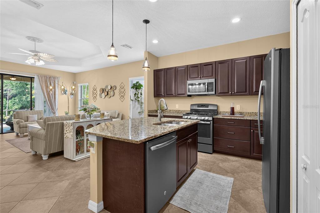 A kitchen with dark wood cabinets, granite countertops, and an island opens to a living area — 11417 OKALOOSA DRIVE, VENICE, FL