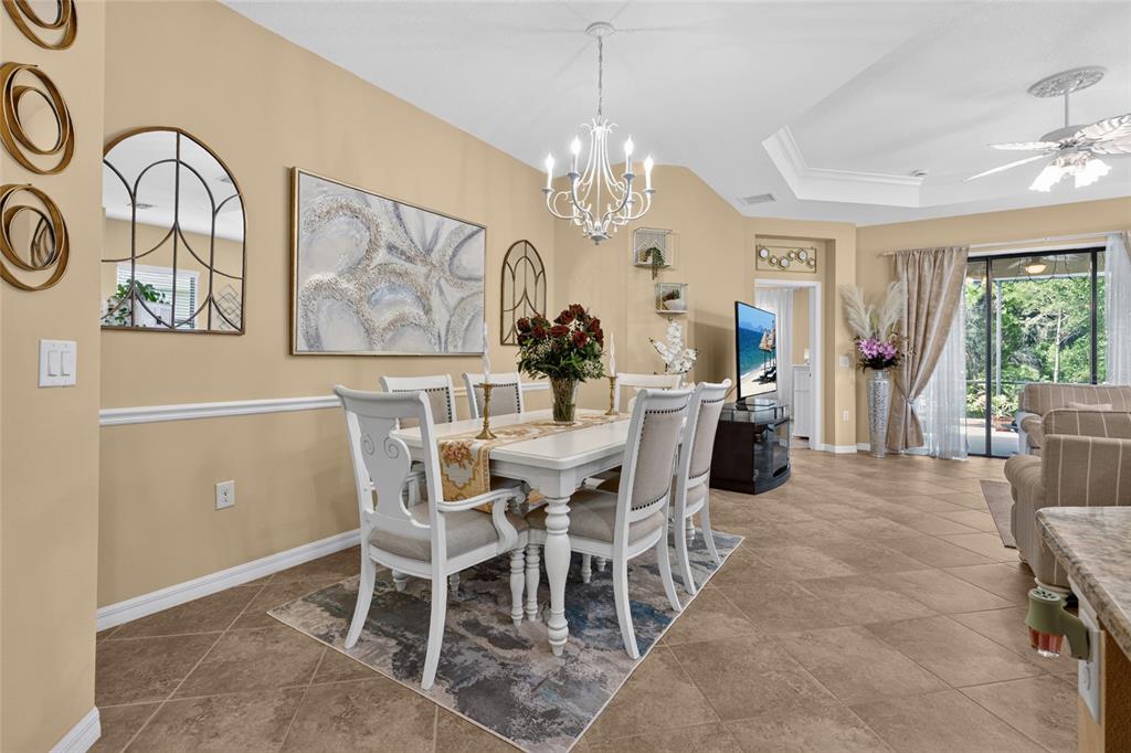 A dining room features a white table, upholstered chairs, a chandelier, and beige tile flooring — 11417 OKALOOSA DRIVE, VENICE, FL