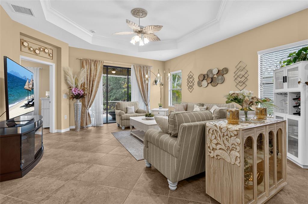 A living room features tile floors, a tray ceiling with a fan, and neutral furniture — 11417 OKALOOSA DRIVE, VENICE, FL