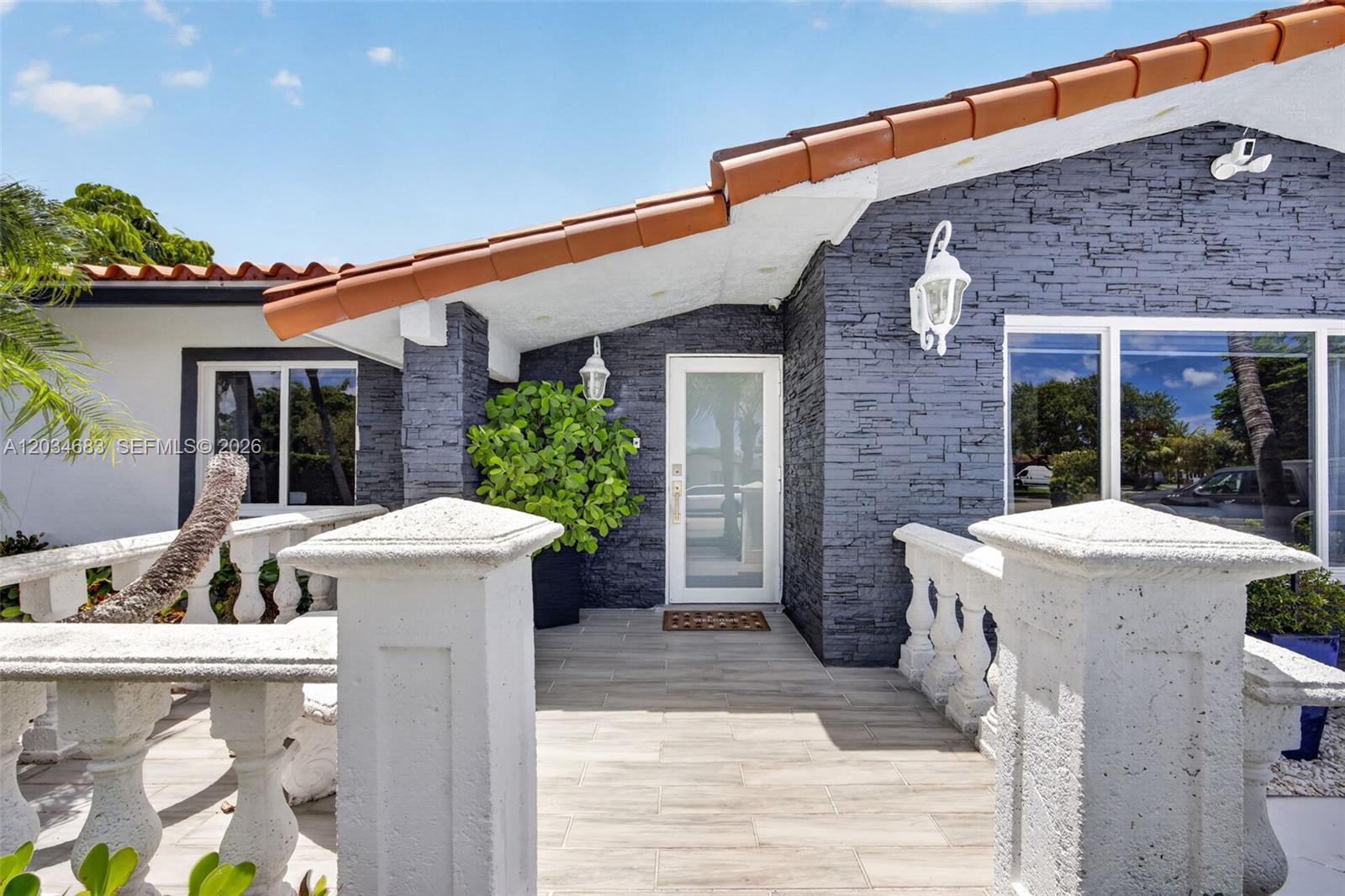 The exterior of a house features a stone-clad entryway, a tiled roof, and white balustrades — 12121 SW 107th St, Miami FL 33186, MIAMI, FL