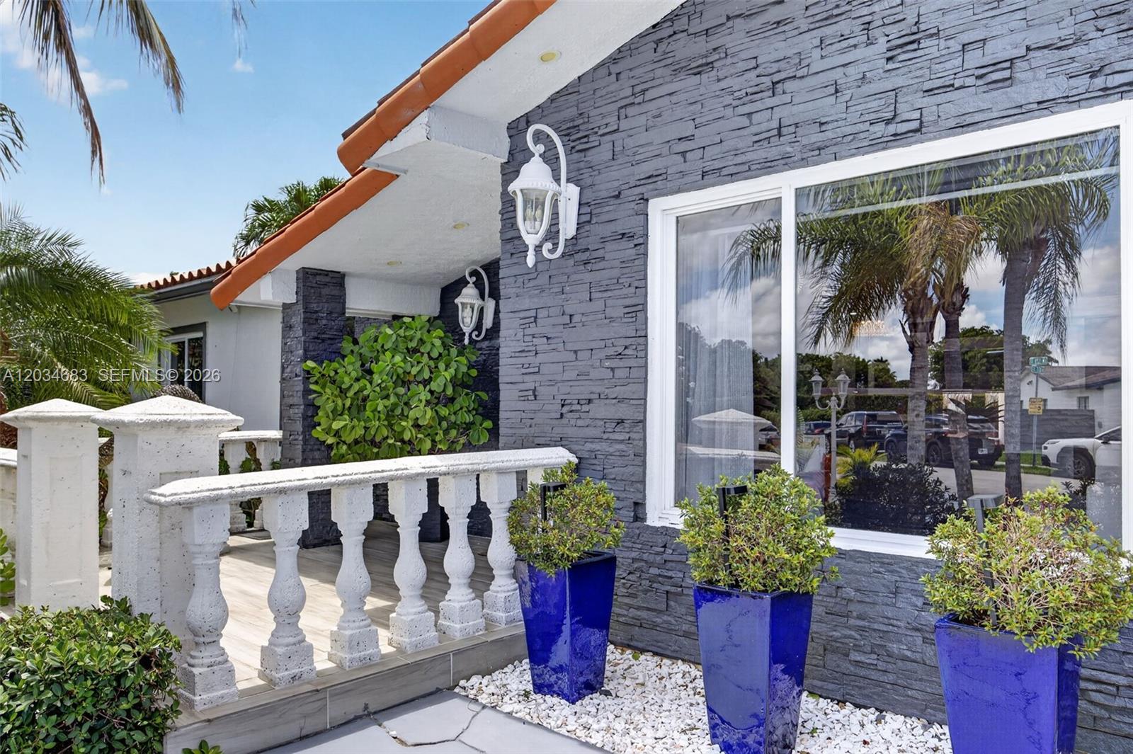 A house exterior features a gray stone facade, white balustrade, and three blue planters — 12121 SW 107th St, Miami FL 33186, MIAMI, FL