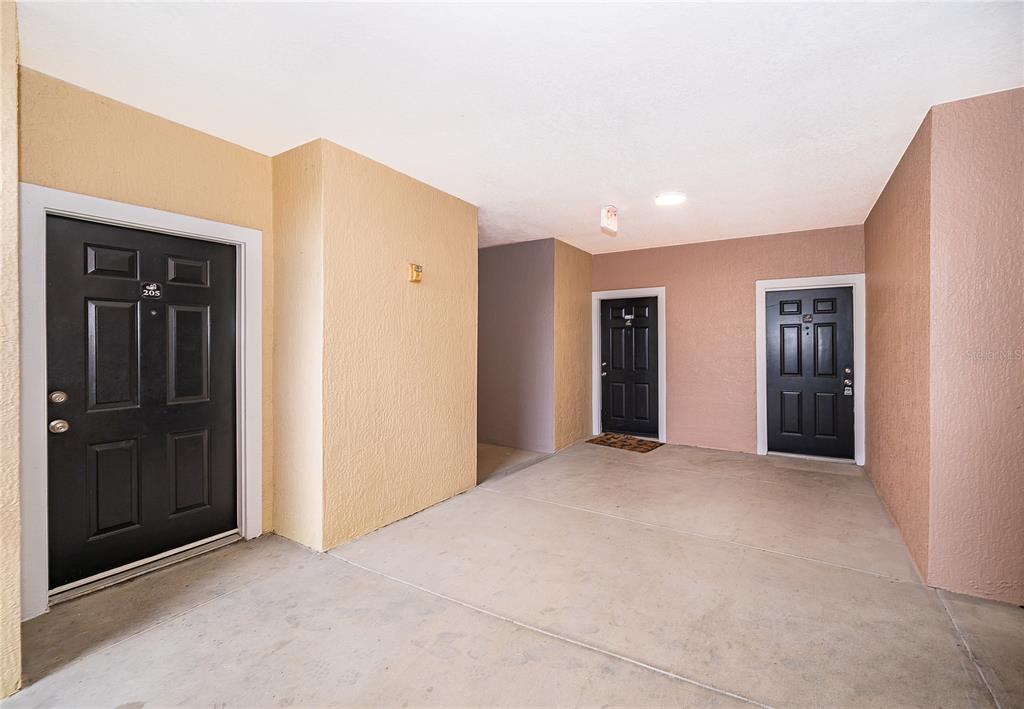 Three black doors are set into beige and pink stucco walls along a concrete walkway — 6663 QUEENS BOROUGH AVENUE UNIT 208, ORLANDO, FL