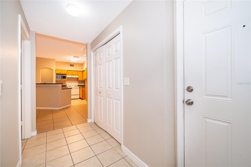 A tiled entryway leads to a kitchen with light wood cabinets and white appliances — 6663 QUEENS BOROUGH AVENUE UNIT 208, ORLANDO, FL