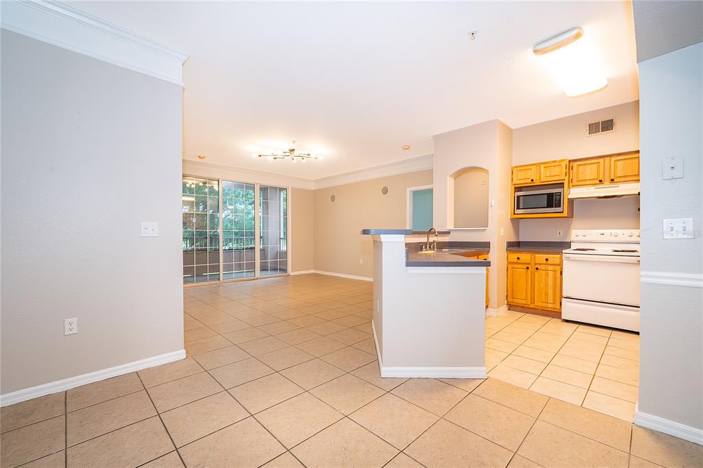 An open-concept kitchen with wood cabinets and tile flooring overlooks a spacious living area — 6663 QUEENS BOROUGH AVENUE UNIT 208, ORLANDO, FL