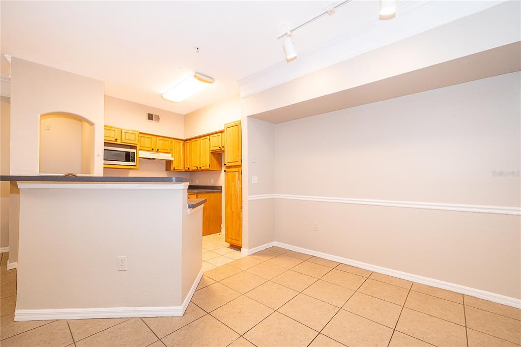 A kitchen with wooden cabinets and a breakfast bar overlooks an open dining area — 6663 QUEENS BOROUGH AVENUE UNIT 208, ORLANDO, FL