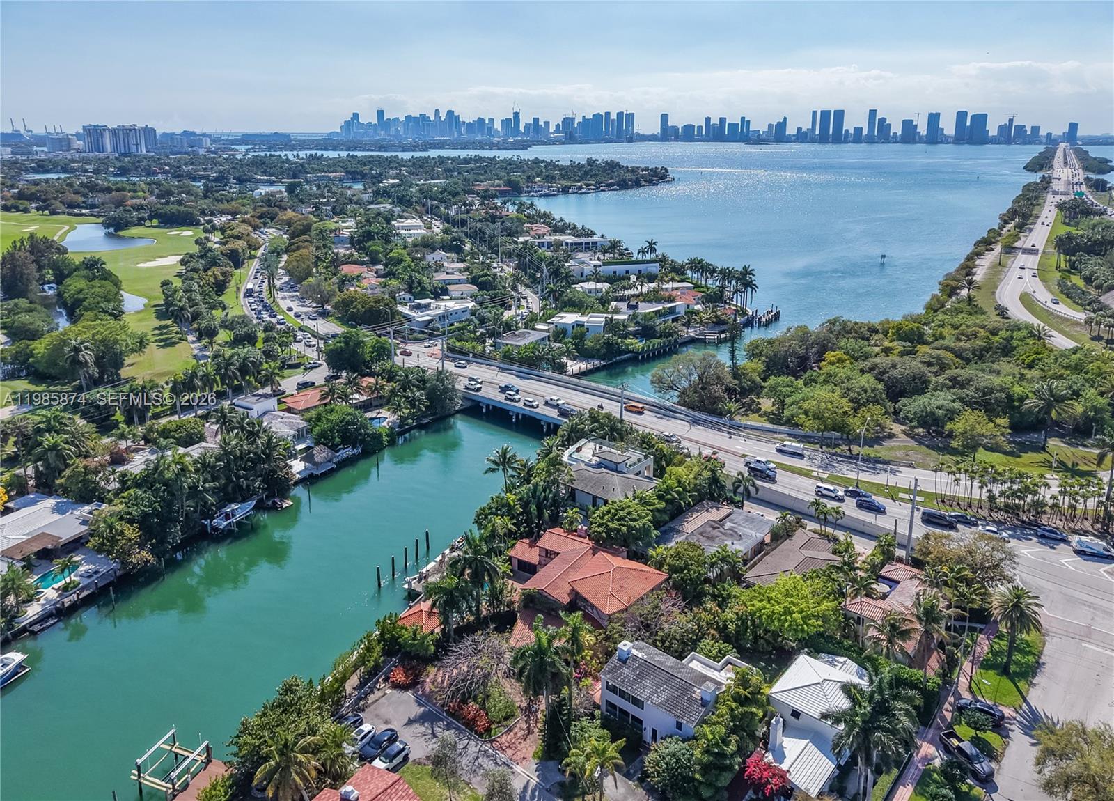 An aerial view shows a canal, a bridge, residential homes, and a distant city skyline — 3310 Garden Ave, Miami Beach FL 33140, MIAMI BEACH, FL