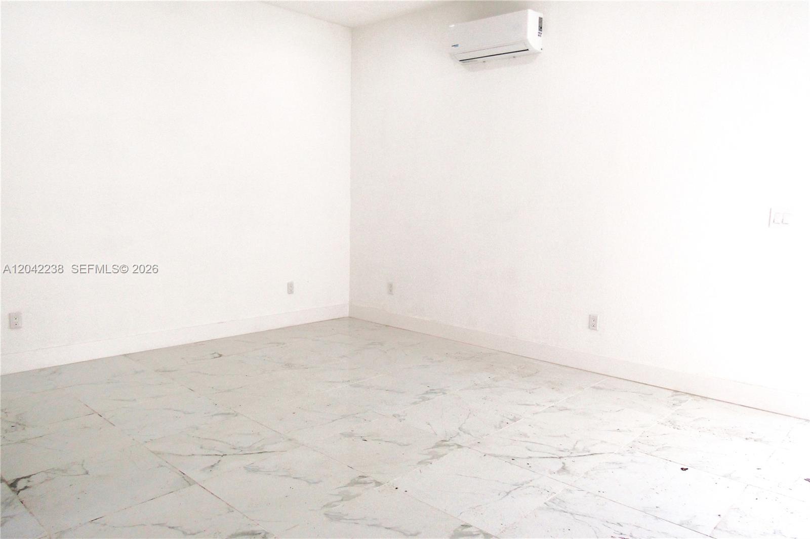 An empty room features white walls, marble-patterned tile flooring, and a wall-mounted air conditioning unit — 15571 SW 183rd Ln # A, Miami FL 33187, MIAMI, FL