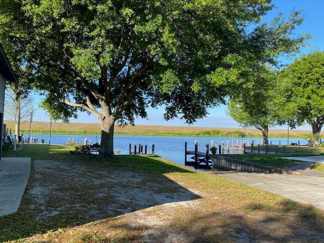 A large tree shades a grassy yard leading to a boat dock on a lake — 8680 Us-441, Okeechobee FL 34974, OKEECHOBEE, FL