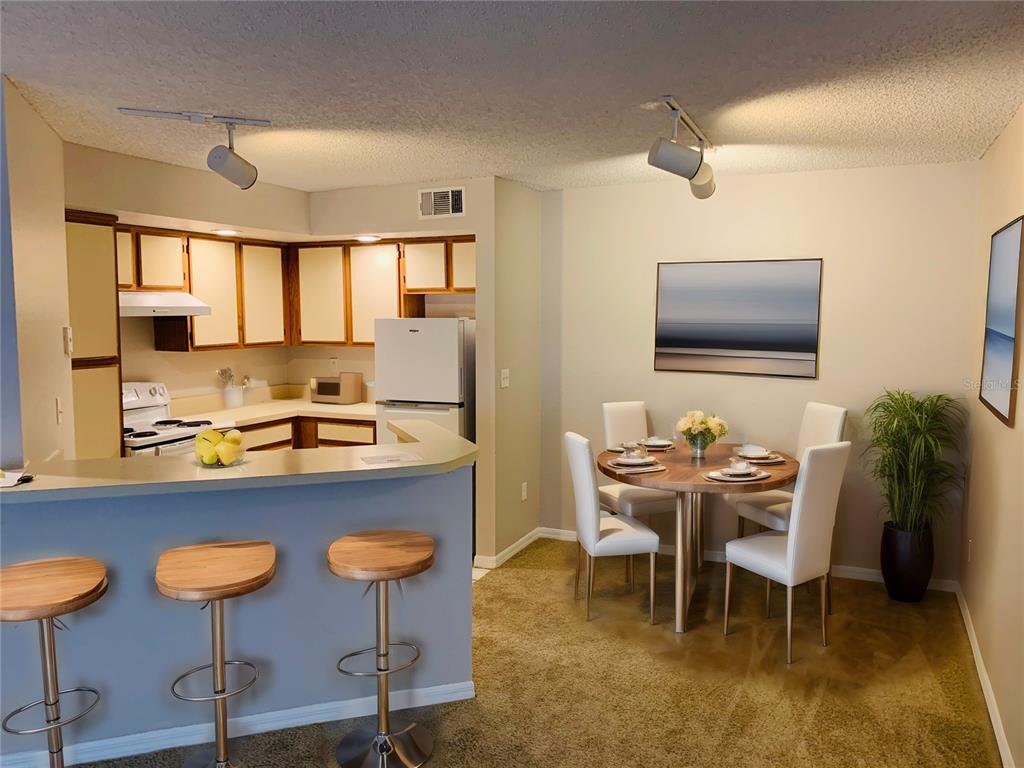 A kitchen with a breakfast bar and stools opens into a dining area with carpet — 4572 COMMANDER DRIVE UNIT 1226, ORLANDO, FL