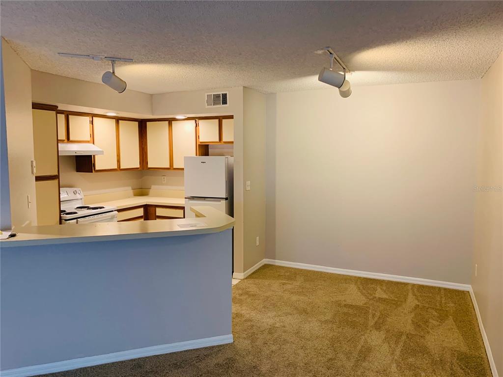 A kitchen with white appliances and cabinets overlooks a carpeted dining area with track lighting — 4572 COMMANDER DRIVE UNIT 1226, ORLANDO, FL