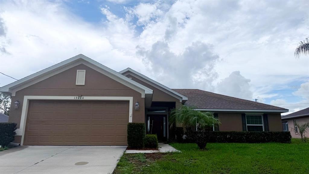 A single-story house with a brown exterior, a two-car garage, and a front lawn — 13064 PIRATE LAKE, SPRING HILL, FL