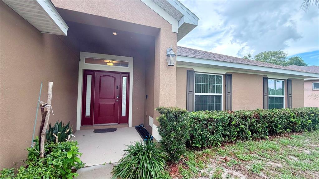 The exterior of a tan house features a red front door and a manicured hedge — 13064 PIRATE LAKE, SPRING HILL, FL