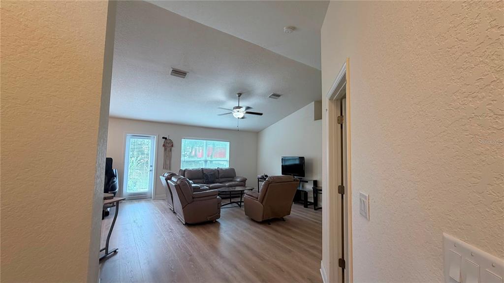 A living room with light wood-look flooring, a ceiling fan, and a vaulted ceiling — 13064 PIRATE LAKE, SPRING HILL, FL