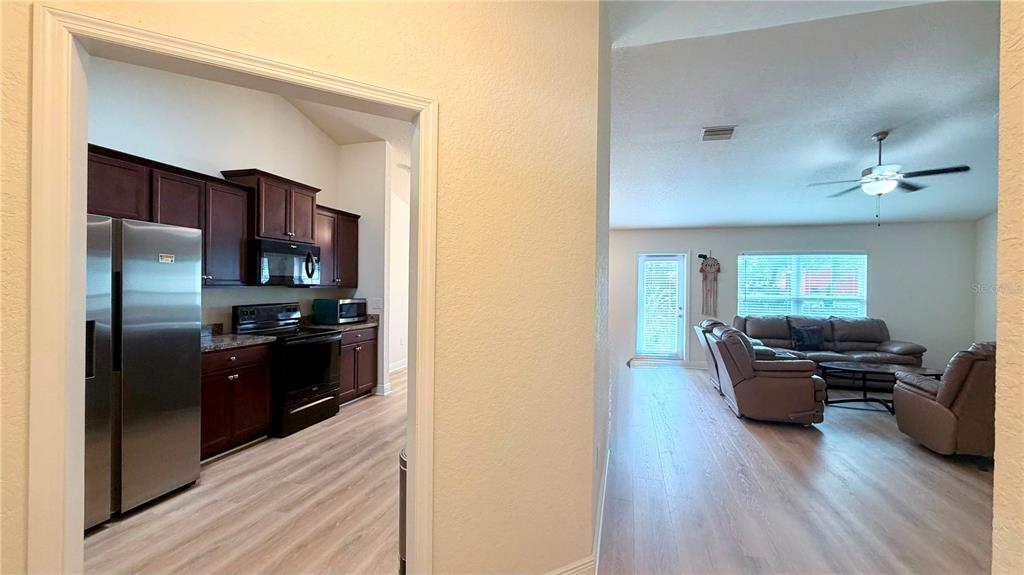 A view through a doorway into a kitchen and an adjacent living room with flooring — 13064 PIRATE LAKE, SPRING HILL, FL