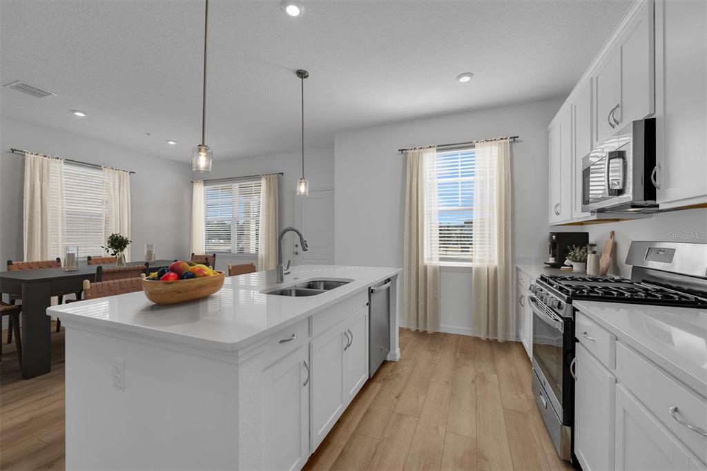 A modern kitchen features a white island with a sink, stainless appliances, and light flooring — 33212 CONTENTMENT WAY, WESLEY CHAPEL, FL