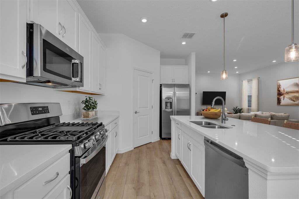 A modern kitchen features white cabinetry, stainless steel appliances, and a central island with seating — 33212 CONTENTMENT WAY, WESLEY CHAPEL, FL