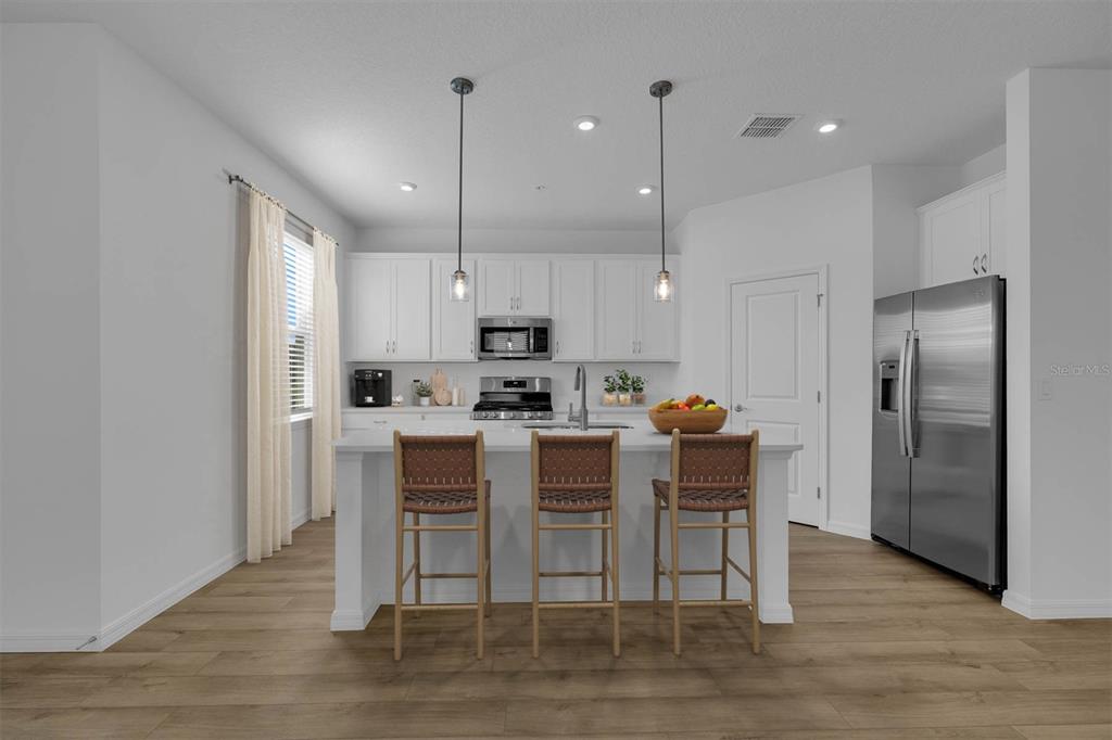 A modern kitchen features white cabinetry, a central island with three stools, and stainless appliances — 33212 CONTENTMENT WAY, WESLEY CHAPEL, FL