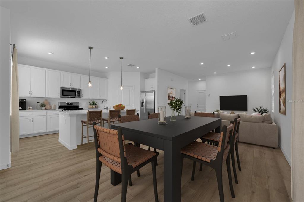 An open-concept kitchen and dining area features white cabinetry, a kitchen island, and wood flooring — 33212 CONTENTMENT WAY, WESLEY CHAPEL, FL