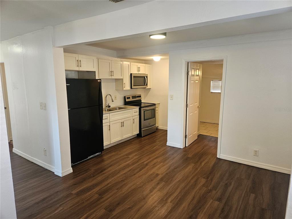 A kitchen features white cabinets, stainless steel appliances, a black refrigerator, and wood-look flooring — 3450 17TH AVENUE S, ST PETERSBURG, FL