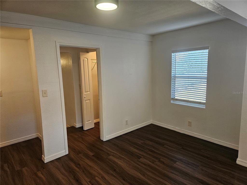 An empty room features dark wood-look flooring, white walls, a window with blinds, and a closet — 3450 17TH AVENUE S, ST PETERSBURG, FL