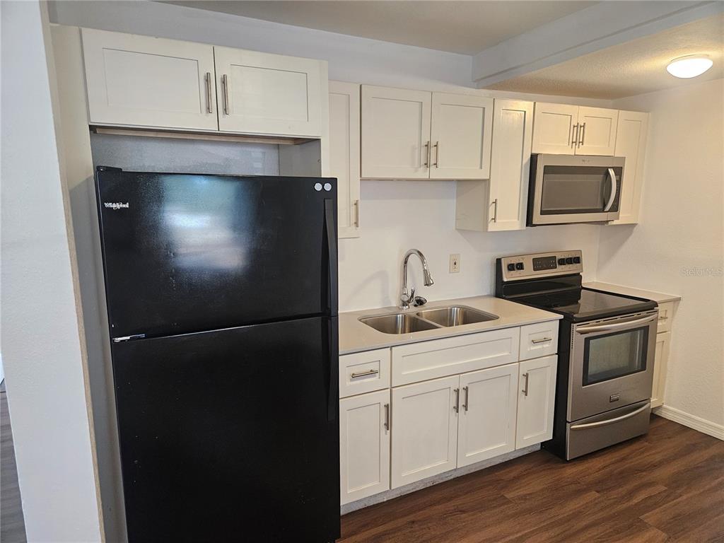 A kitchen features white cabinets, a black refrigerator, stainless steel appliances, and wood-look flooring — 3450 17TH AVENUE S, ST PETERSBURG, FL