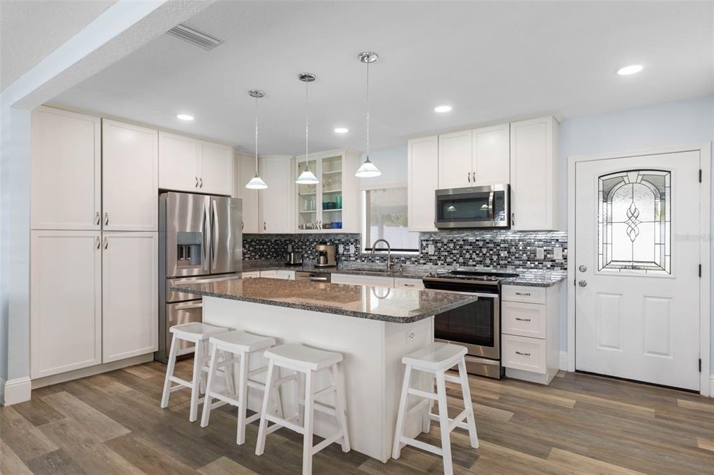 A kitchen features white cabinetry, granite countertops, a central island with stools, and stainless appliances — 26 OCEAN VISTA LANE, PALM COAST, FL