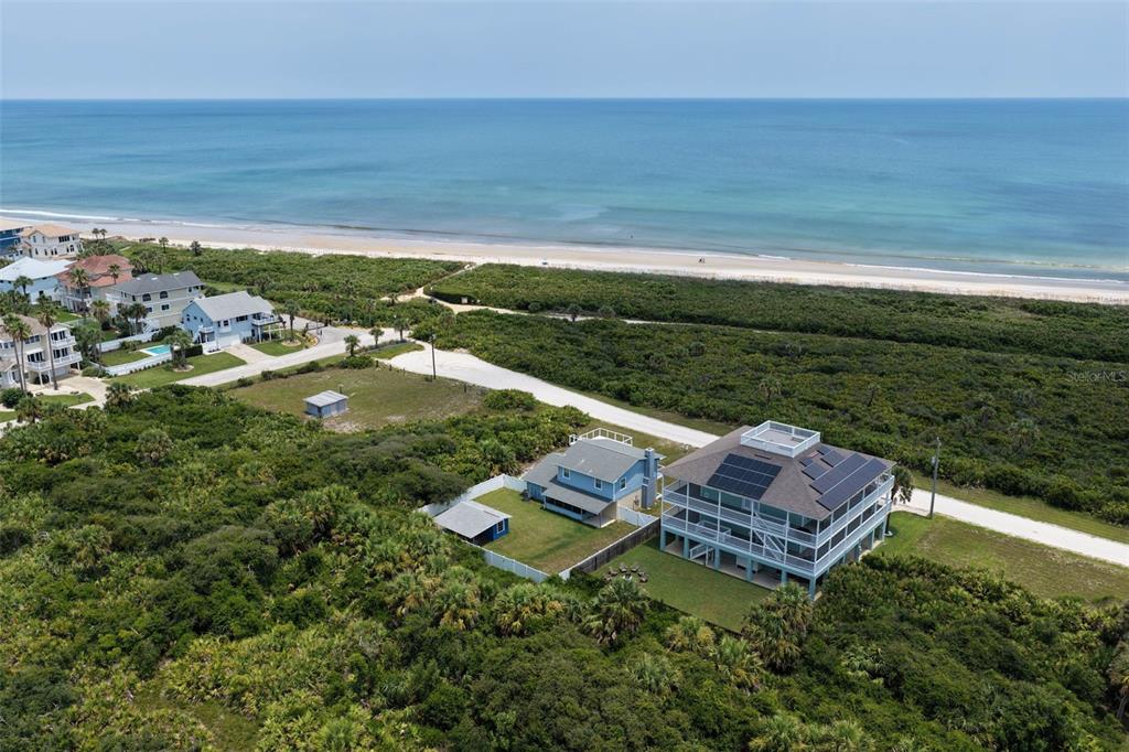 An aerial view shows a multi-story house with solar panels near a beach and vegetation — 26 OCEAN VISTA LANE, PALM COAST, FL