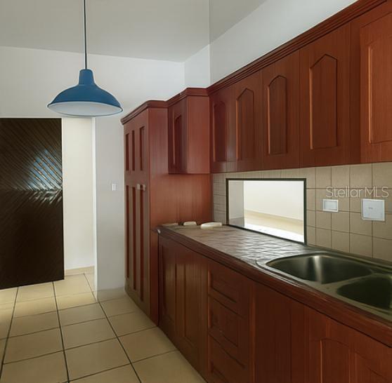 A kitchen features wood cabinets, a stainless steel sink, a blue pendant light, and tile floors — 3 CLARISA STREET UNIT 447, PONCE, PR