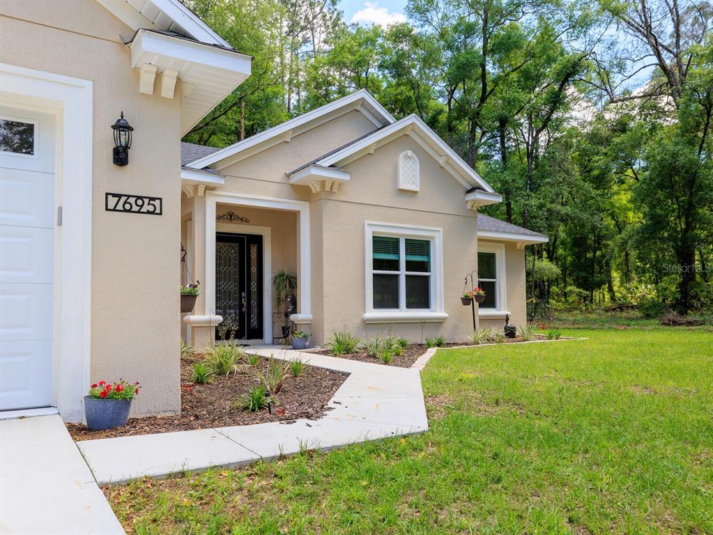 A tan stucco house exterior features a front entrance, a garage, and a landscaped yard — 7695 SW 188TH AVENUE, DUNNELLON, FL