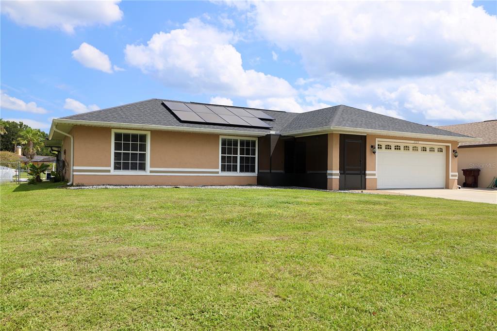 A single-story house with a tan exterior, a shingled roof with solar panels, and a garage — 1123 ANNE ELISA CIRCLE, ST CLOUD, FL