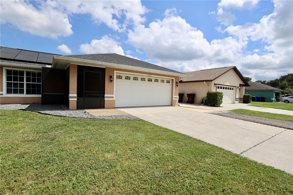 A tan single-story house with a white garage door and a screened-in front entryway — 1123 ANNE ELISA CIRCLE, ST CLOUD, FL