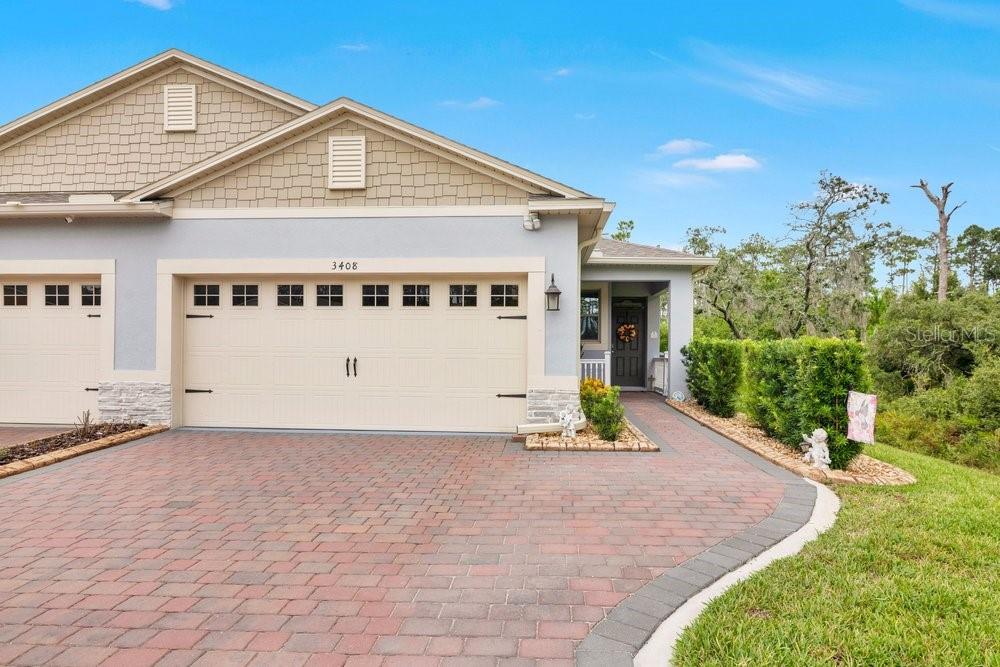 A suburban house exterior features a two-car garage, a brick driveway, and a covered entryway — 3408 TWIN FLOWER COURT, CLERMONT, FL
