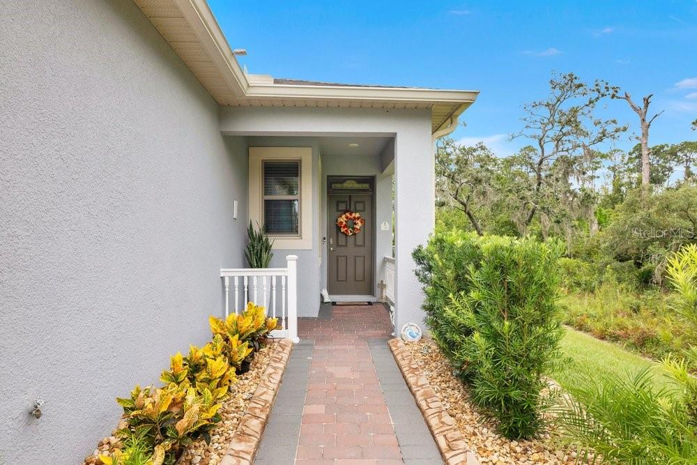 A paved walkway leads to the covered front entrance of a house with gray stucco siding — 3408 TWIN FLOWER COURT, CLERMONT, FL