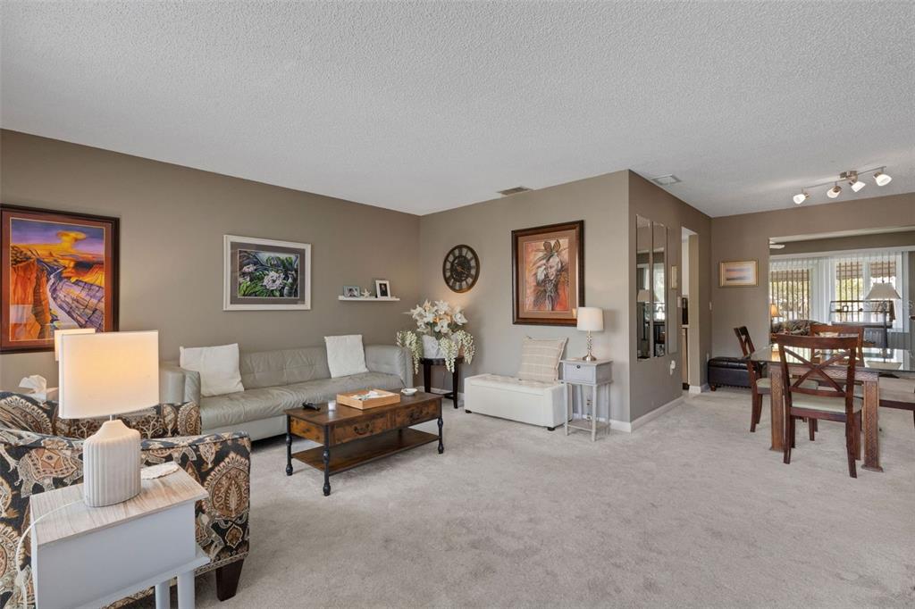 A living room with beige carpet, a grey sofa, a coffee table, and a dining area — 1306 BOTTLEBRUSH DRIVE, BRADENTON, FL