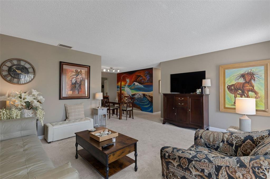 A living room features beige carpet, neutral walls, a dark wood media console, and artwork — 1306 BOTTLEBRUSH DRIVE, BRADENTON, FL