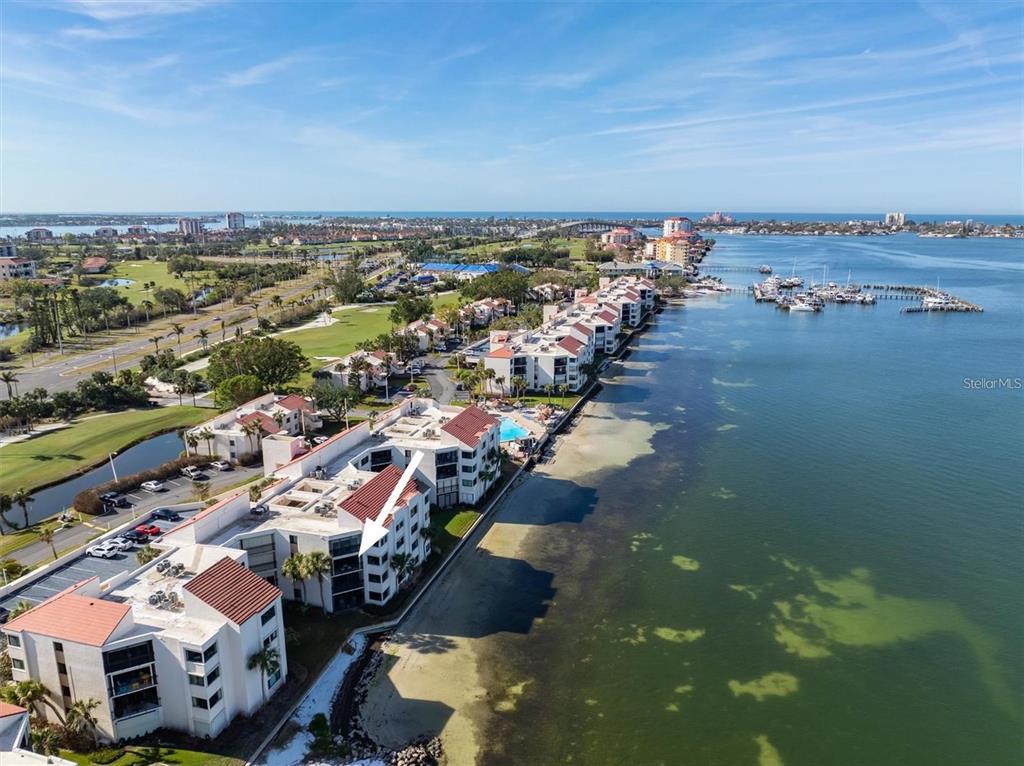 An aerial view shows waterfront condominium buildings with a white arrow pointing to a unit — 5633 PUERTA DEL SOL BOULEVARD S UNIT 307, ST PETERSBURG, FL