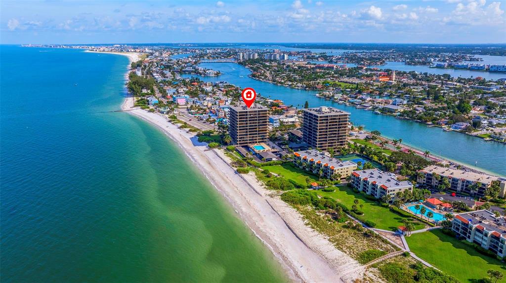 An aerial view shows high-rise condominiums situated along a sandy beach and coastal waterway — 7650 BAYSHORE DRIVE UNIT 1005, TREASURE ISLAND, FL