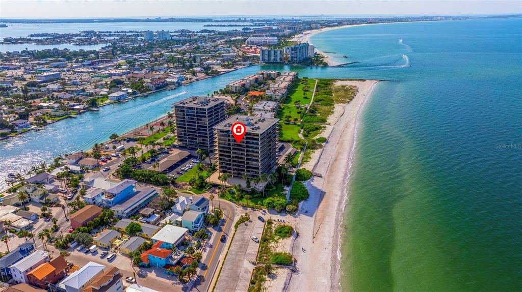 An aerial view shows a multi-story apartment building situated on a beach near water — 7650 BAYSHORE DRIVE UNIT 1005, TREASURE ISLAND, FL