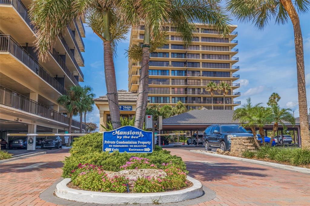 A gated entrance with a sign for a condominium complex features palm trees and buildings — 7650 BAYSHORE DRIVE UNIT 1005, TREASURE ISLAND, FL