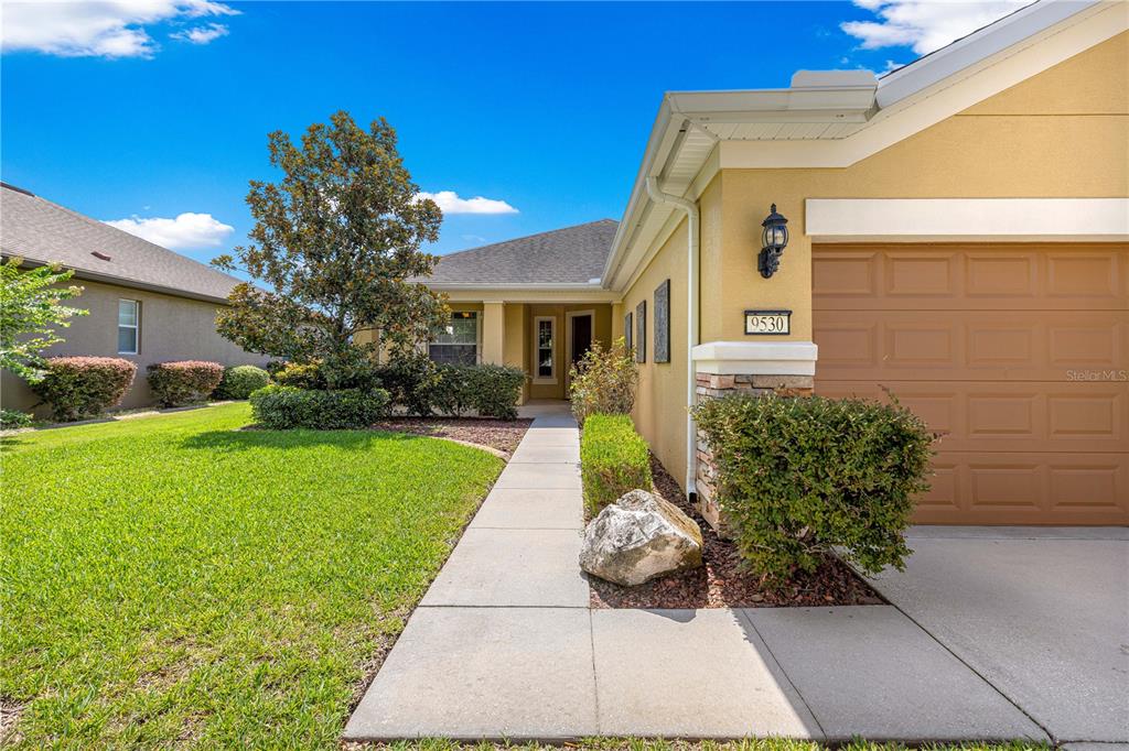 A concrete walkway leads to the front entrance of a yellow house with a garage — 9530 SW 70TH LOOP, OCALA, FL