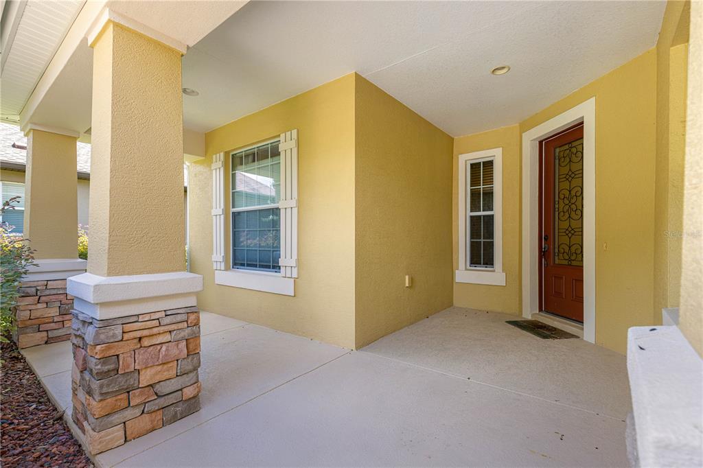 A covered front porch features yellow stucco walls, a stone-based pillar, and a brown door — 9530 SW 70TH LOOP, OCALA, FL