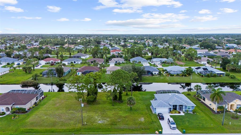 An aerial view shows a vacant residential lot situated between two houses along a canal — 29 MARKER ROAD, ROTONDA WEST, FL
