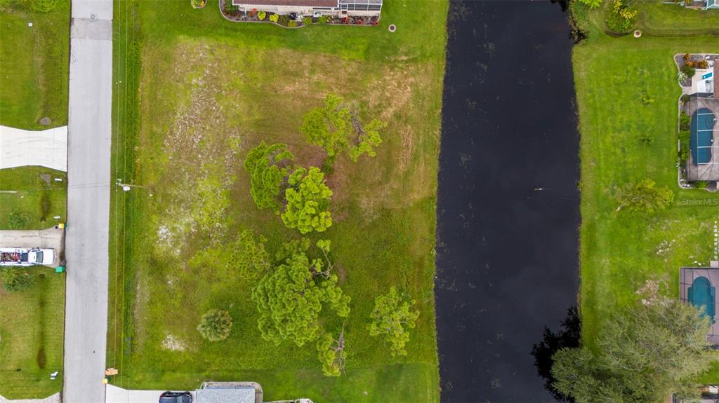 An aerial view shows a vacant, grassy residential lot situated between a road and a canal — 29 MARKER ROAD, ROTONDA WEST, FL