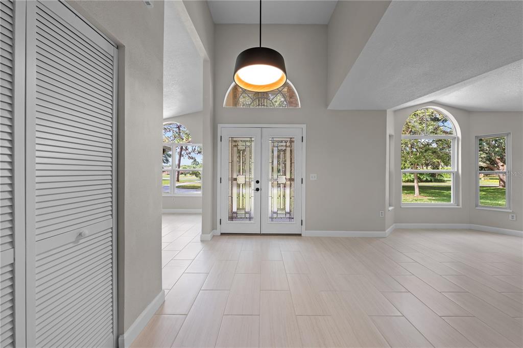An entryway with light tile floors, a high ceiling, a pendant light, and double glass doors — 2082 CAMELOT BOULEVARD, ST CLOUD, FL